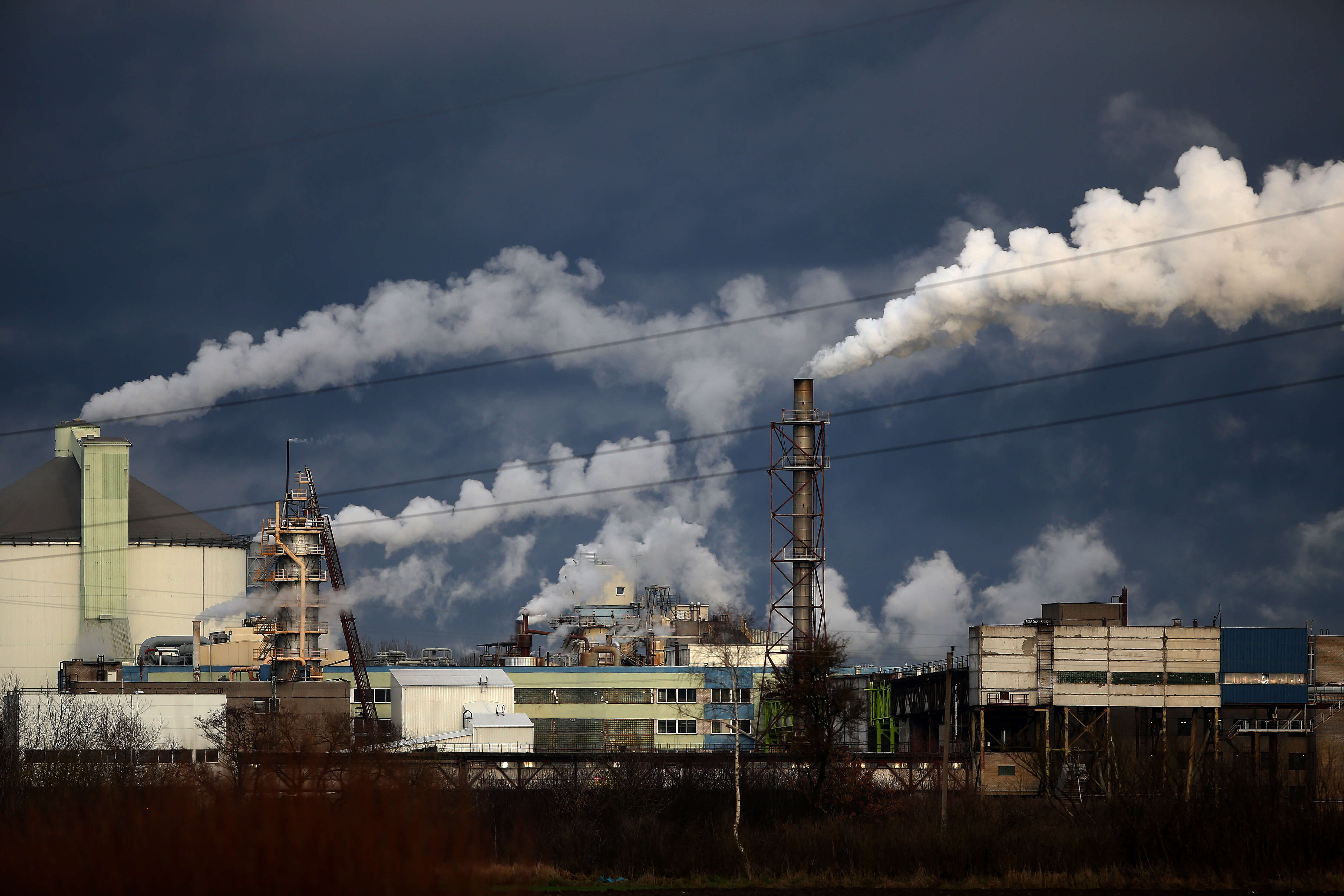 Large industrial factory operating at high production capacity with visible emissions and heavy manufacturing infrastructure