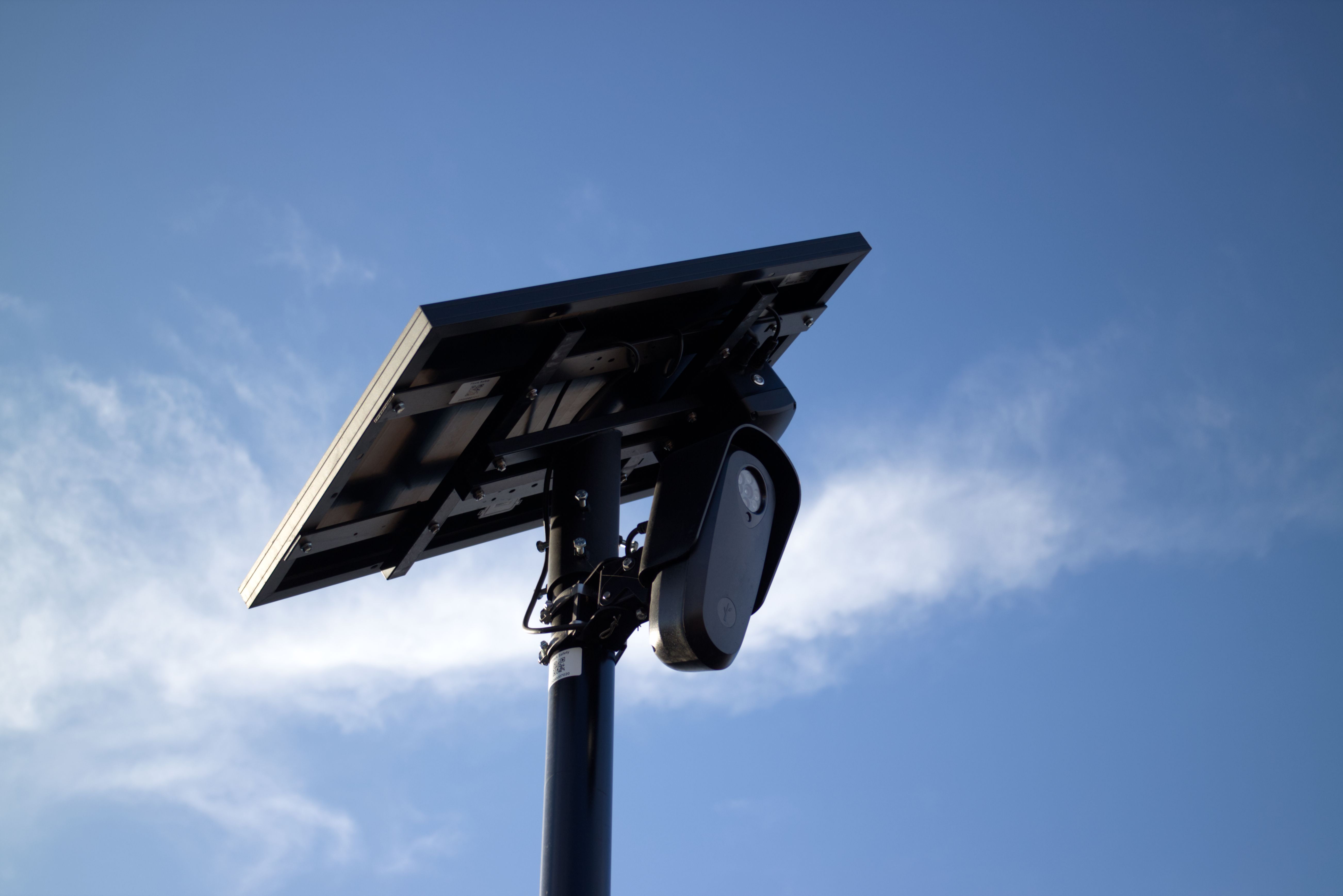 Solar panel and security camera mounted on a pole against a blue sky