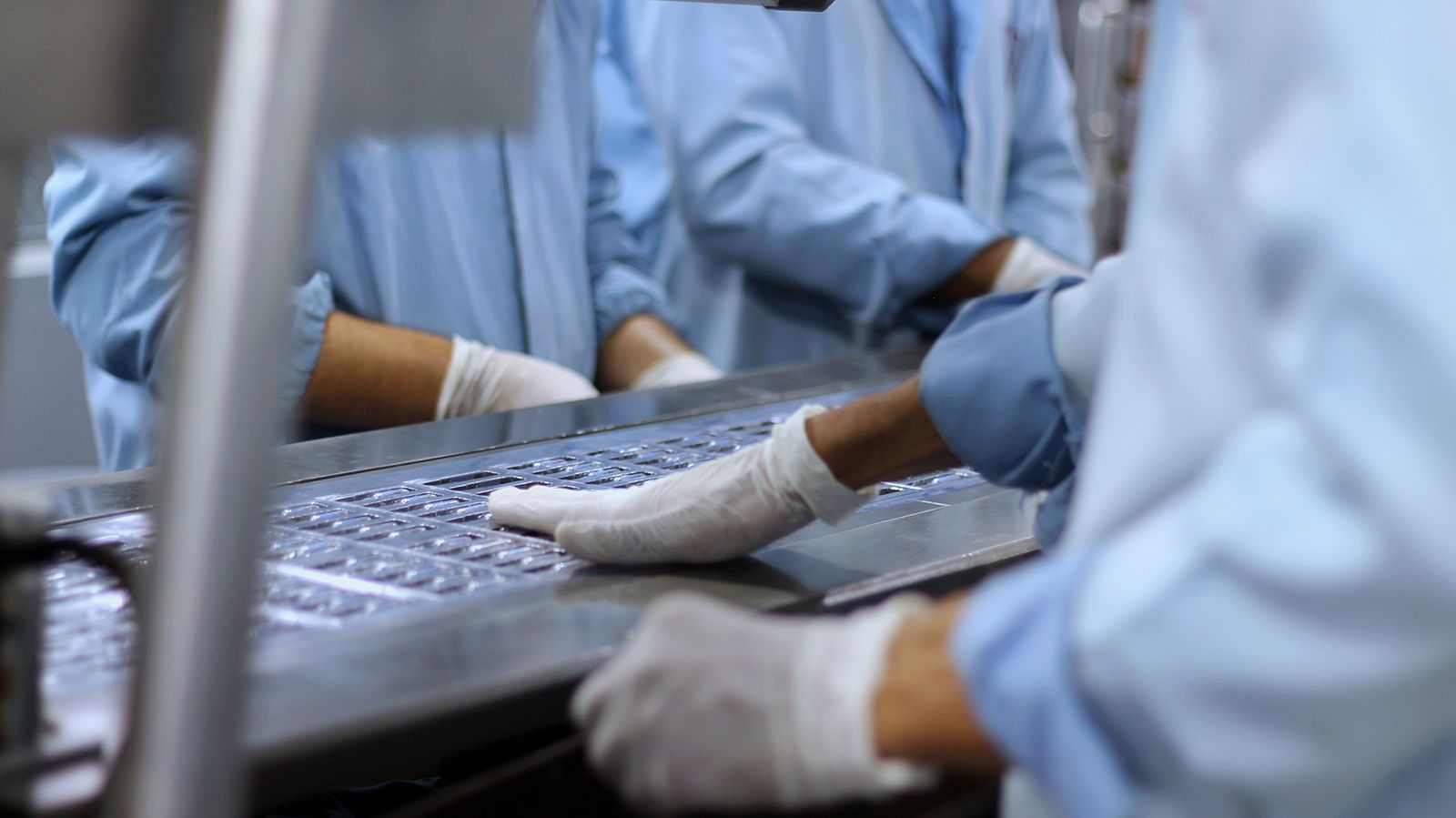 Workers in cleanroom gowns and gloves operating equipment on a production line